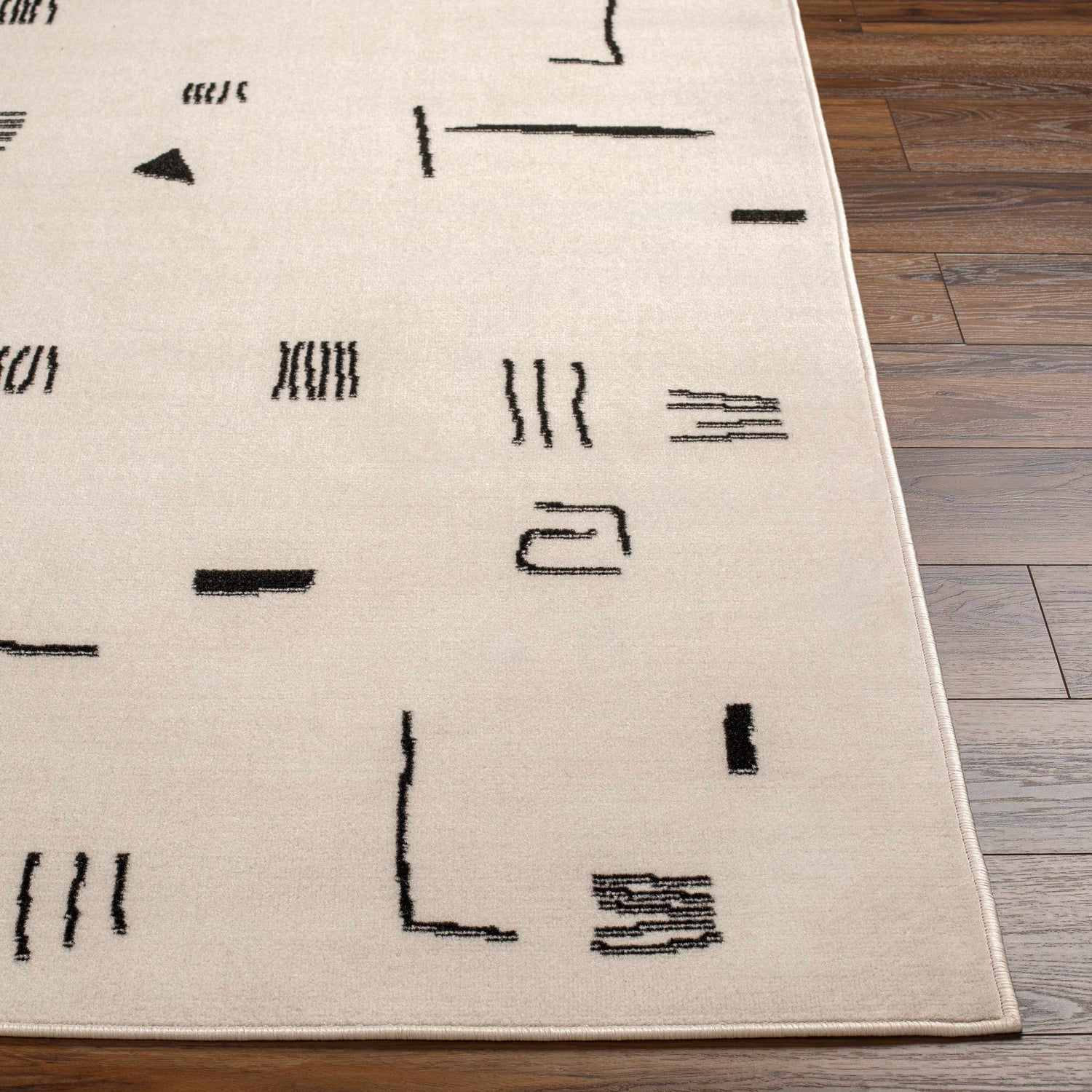 Close up of the Zale Area Rug showing a bone color with a dark gray, geometric pattern. Front
